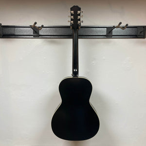 An Epiphone L-00 Standard Vintage Sunburst acoustic guitar hangs by its headstock on a wall-mounted rack, back facing out, against a plain white wall. Gigbag included.