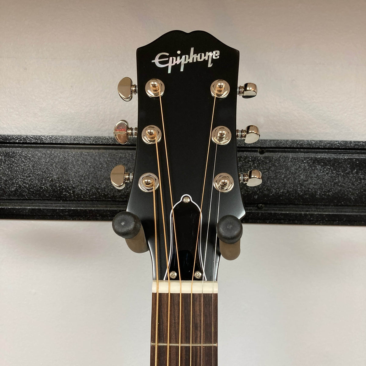 Close-up of the headstock of an Epiphone L-00 Standard Vintage Sunburst w/Gigbag, a small-bodied acoustic by Epiphone, with six tuning pegs, hanging on a wall-mounted guitar holder.