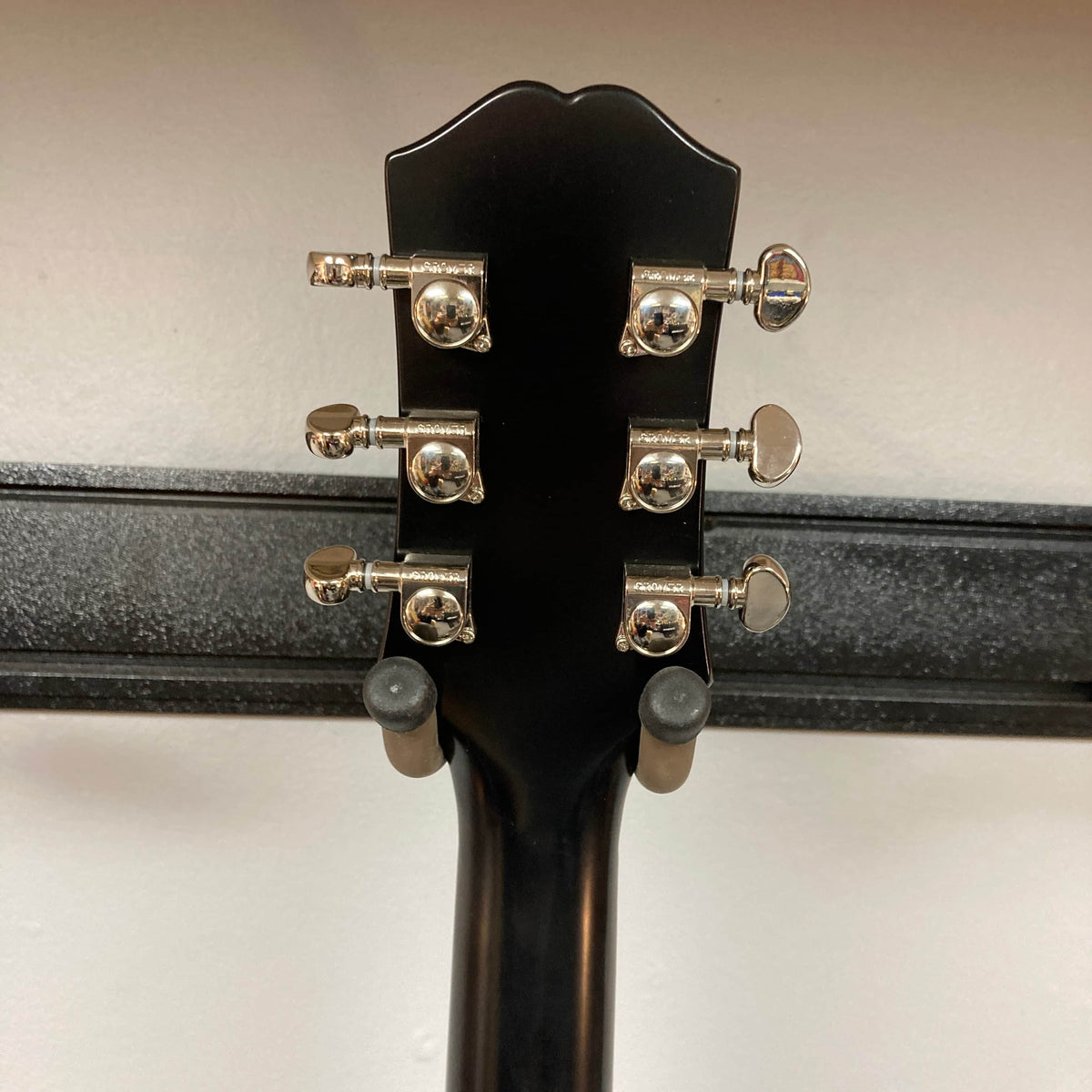 Rear view of the Epiphone L-00 Standard Vintage Sunburst w/Gigbag headstock, featuring six chrome tuners, with this small-bodied acoustic guitar by Epiphone resting on a wall-mounted hanger.
