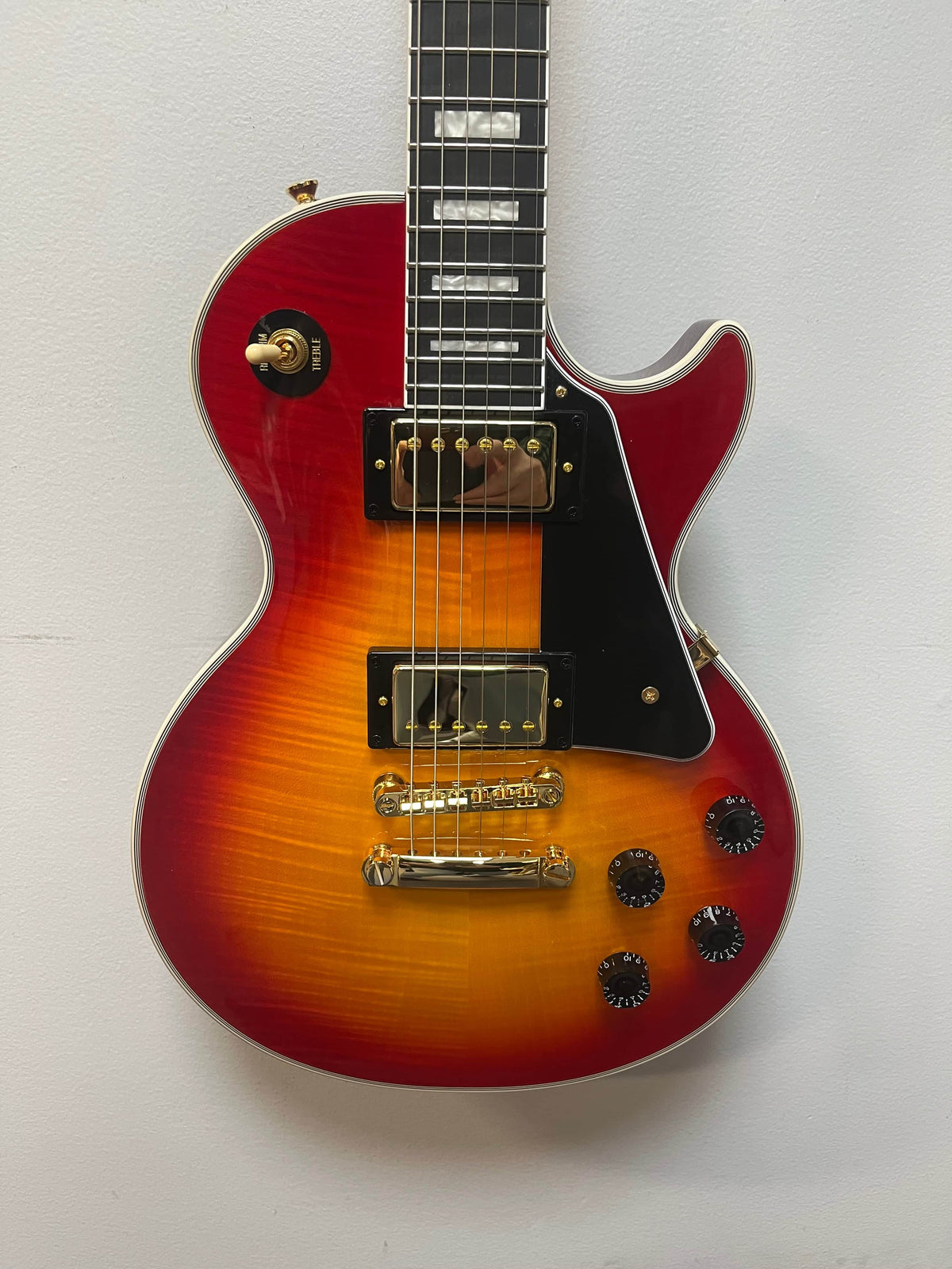 An Epiphone Les Paul Custom, Heritage Cherry Sunburst, Exclusive by Epiphone with gold hardware, black pickguard, four control knobs, and dual ProBucker humbuckers hangs against a plain white wall.