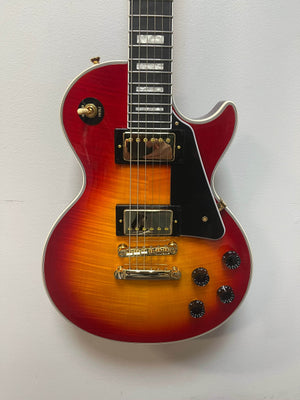 An Epiphone Les Paul Custom, Heritage Cherry Sunburst, Exclusive by Epiphone with gold hardware, black pickguard, four control knobs, and dual ProBucker humbuckers hangs against a plain white wall.