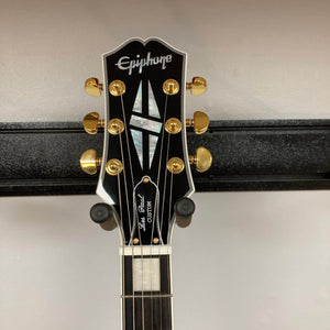 Close-up of the headstock of the Epiphone Les Paul Custom, Heritage Cherry Sunburst (Exclusive w/GigBag) electric guitar, showing gold tuners, pearl inlays, and “Epiphone” and “Les Paul Custom” logos.