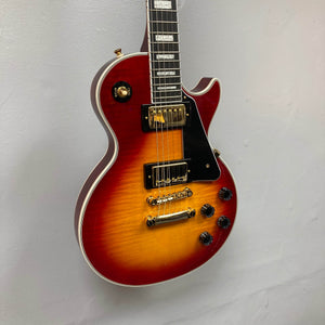 A close-up of the Epiphone Les Paul Custom, Heritage Cherry Sunburst (Exclusive w/GigBag), highlights its gold hardware, black pickguard, four control knobs, and ProBucker humbuckers against a plain light gray wall.