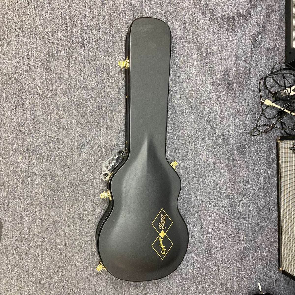 Epiphone Les Paul Custom Inspired by Gibson Ebony w/Case, featuring a black guitar case with gold trim, displayed on a carpet.