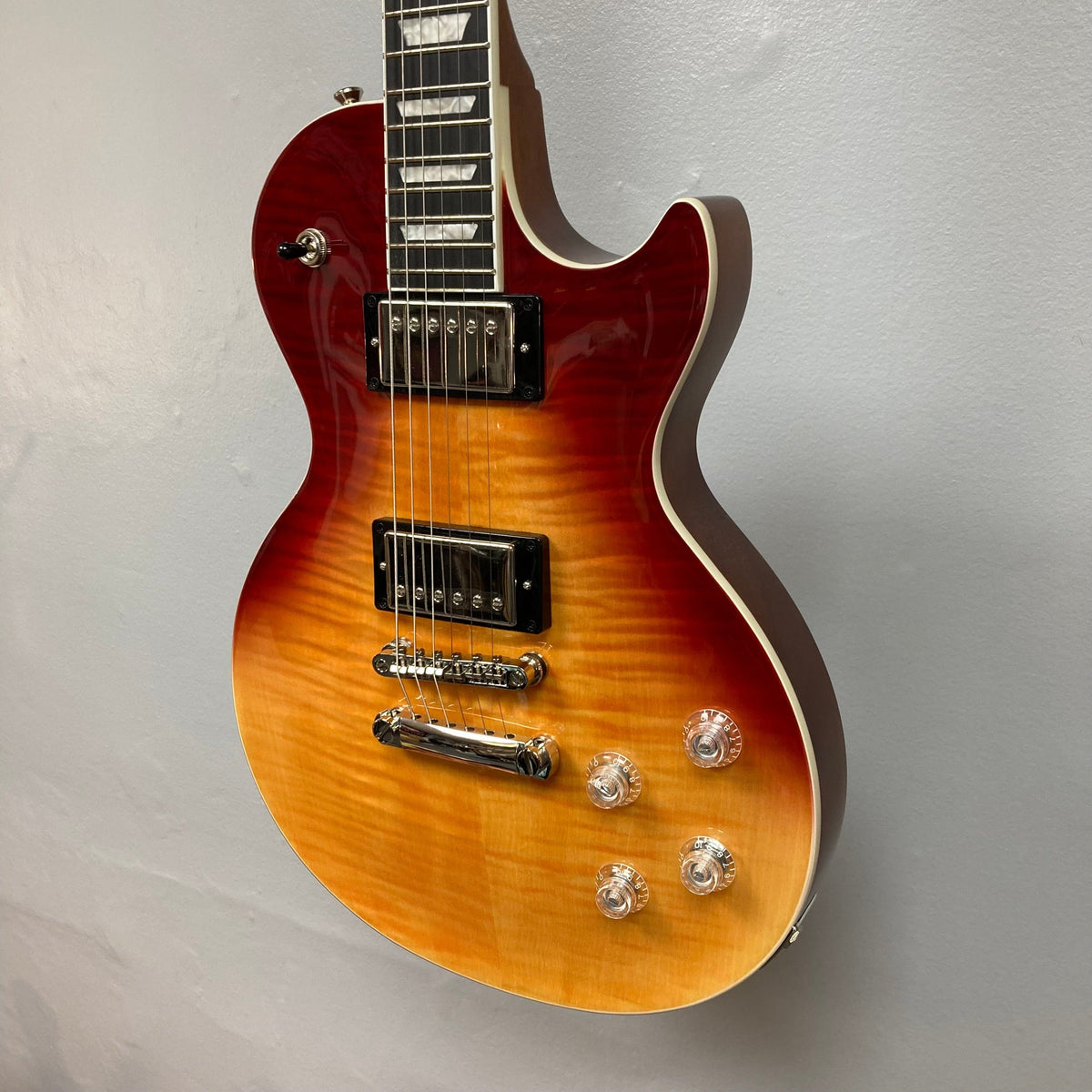 Epiphone Les Paul Modern Figured Magma Orange Fade guitar with visible ProBucker pickups and controls, displayed on a wall.