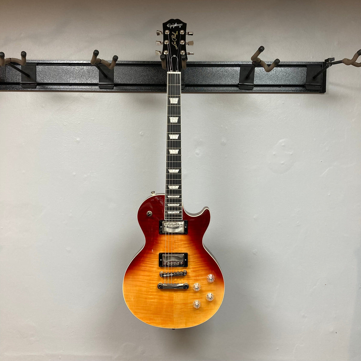 Epiphone Les Paul Modern Figured in Magma Orange Fade, displayed on a wall, showcasing its maple top, dual ProBucker pickups, and sleek design.