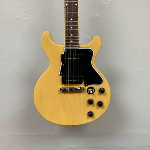 An Epiphone Les Paul Special Double Cut TV Yellow electric guitar with double-cutaway body, black pickguard, four control knobs, and two pickups stands vertically against a plain light-colored wall. Includes gigbag.