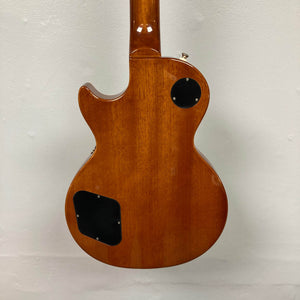 The back of an Epiphone Les Paul Standard 60s Ebony w/Gigbag electric guitar, featuring two black plastic covers, is displayed against a plain light-colored wall.