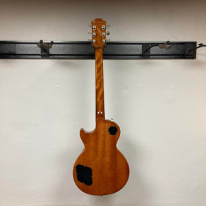 An Epiphone Les Paul Standard 60s Ebony w/Gigbag hangs with its back forward on a black metal rack, showing two control cavity covers.