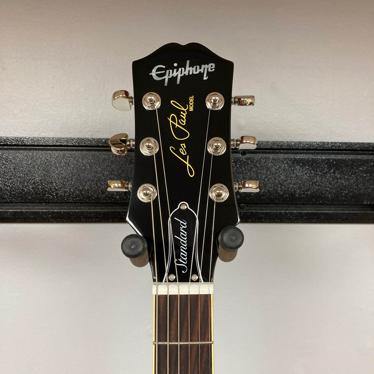 Headstock of the Epiphone Les Paul Standard 60s Ebony w/Gigbag by Epiphone, with tuning pegs, logo, and fretboard visible—a classic nod to vintage Gibson Les Paul design, set against a plain wall.