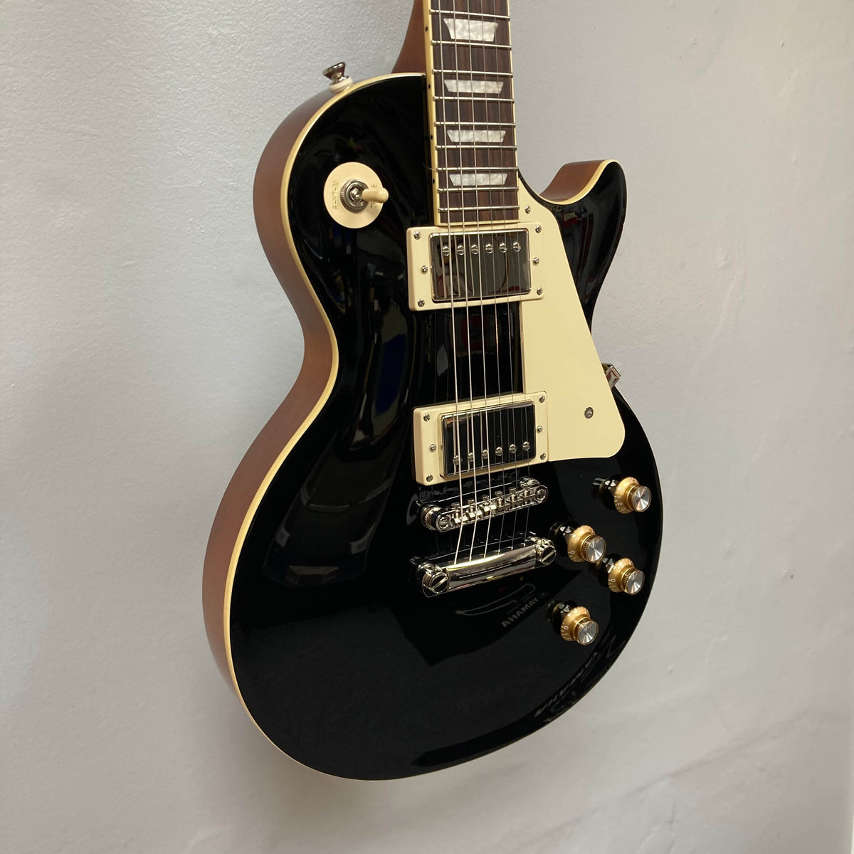 An Epiphone Les Paul Standard 60s Ebony electric guitar, featuring a single cutaway and chrome hardware, is mounted on a white wall.