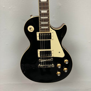An Epiphone Les Paul Standard 60s Ebony electric guitar with a white pickguard, two humbuckers, four control knobs, and a selector switch is shown against a plain light wall. Brand: Epiphone. Includes gigbag.