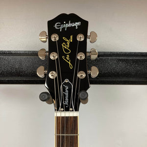 Close-up of the Epiphone Les Paul Standard 60s Figured Iced Tea Burst headstock, showing tuning pegs and logos against a plain background, highlights its classic design. Includes gigbag.