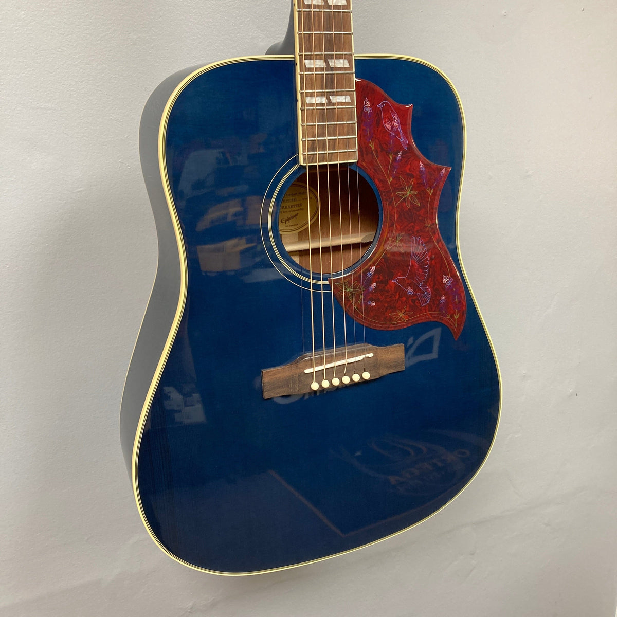 Epiphone Miranda Lambert Bluebird Studio guitar featuring a vivid blue design with red details, inspired by female artists, displayed on a wall.