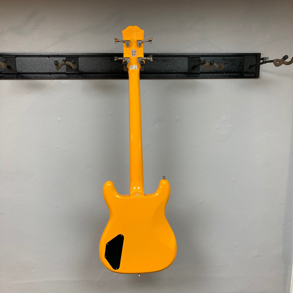 Epiphone Newport Bass California Coral, a yellow electric guitar displayed on a wall, featuring a unique body shape and vintage-inspired design.