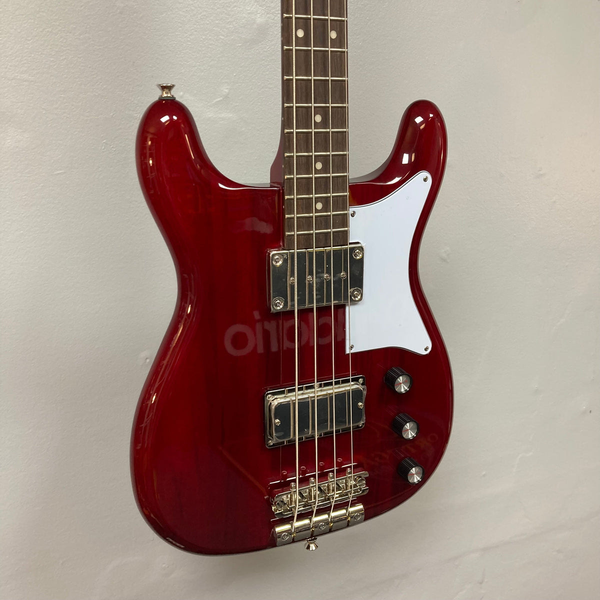 Epiphone Newport Bass Cherry, a vintage-style electric guitar with a mahogany body, visible humbuckers, and control knobs, mounted on a wall.