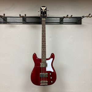 Epiphone Newport Bass Cherry, a vintage-style bass guitar with a distinct body shape, displayed on a wall, showcasing its mahogany construction and control knobs.