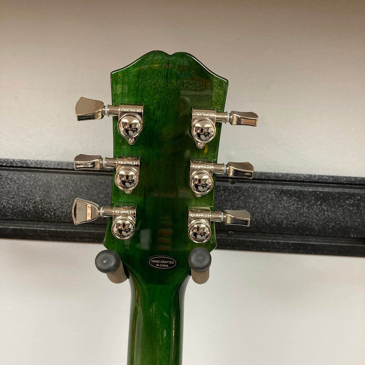 Close-up of the back of an Epiphone SG Modern Figured Iguana Burst headstock with chrome skull-design tuning pegs, mounted on a wall hanger.