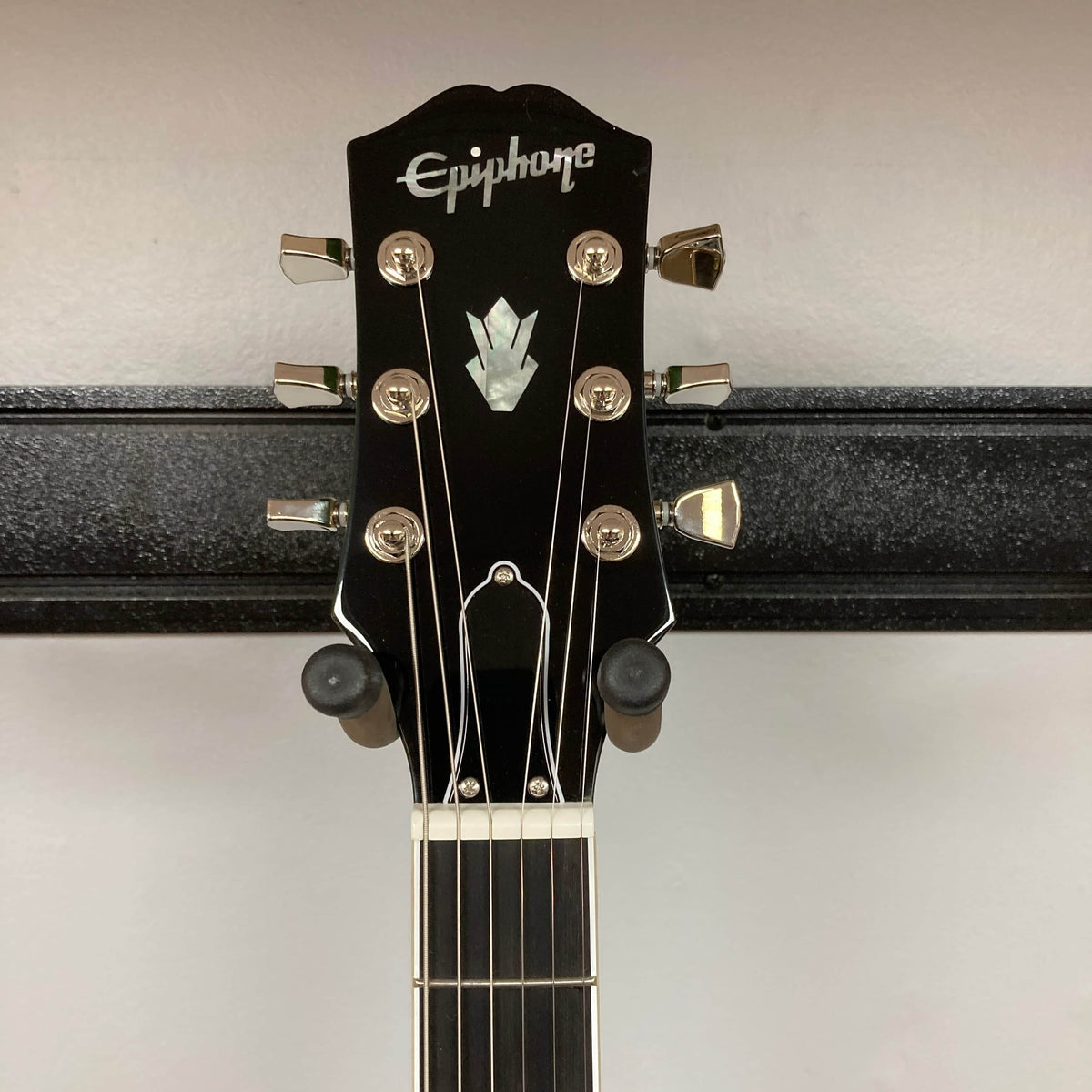 The Epiphone SG Modern Figured Iguana Burst w/GigBag features six tuning pegs on its headstock and a SlimTaper neck, shown hanging on a black wall-mounted guitar holder.
