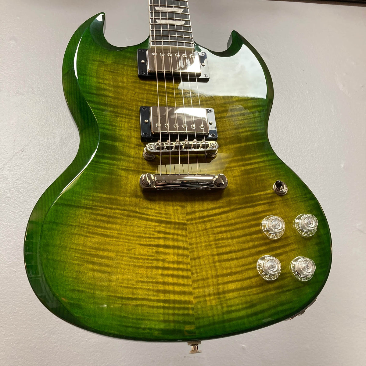 An Epiphone SG Modern Figured electric guitar in Iguana Burst with ProBucker humbuckers, four control knobs, a flamed maple top, and a tune-o-matic bridge is pictured against a plain background. Comes with gig bag.
