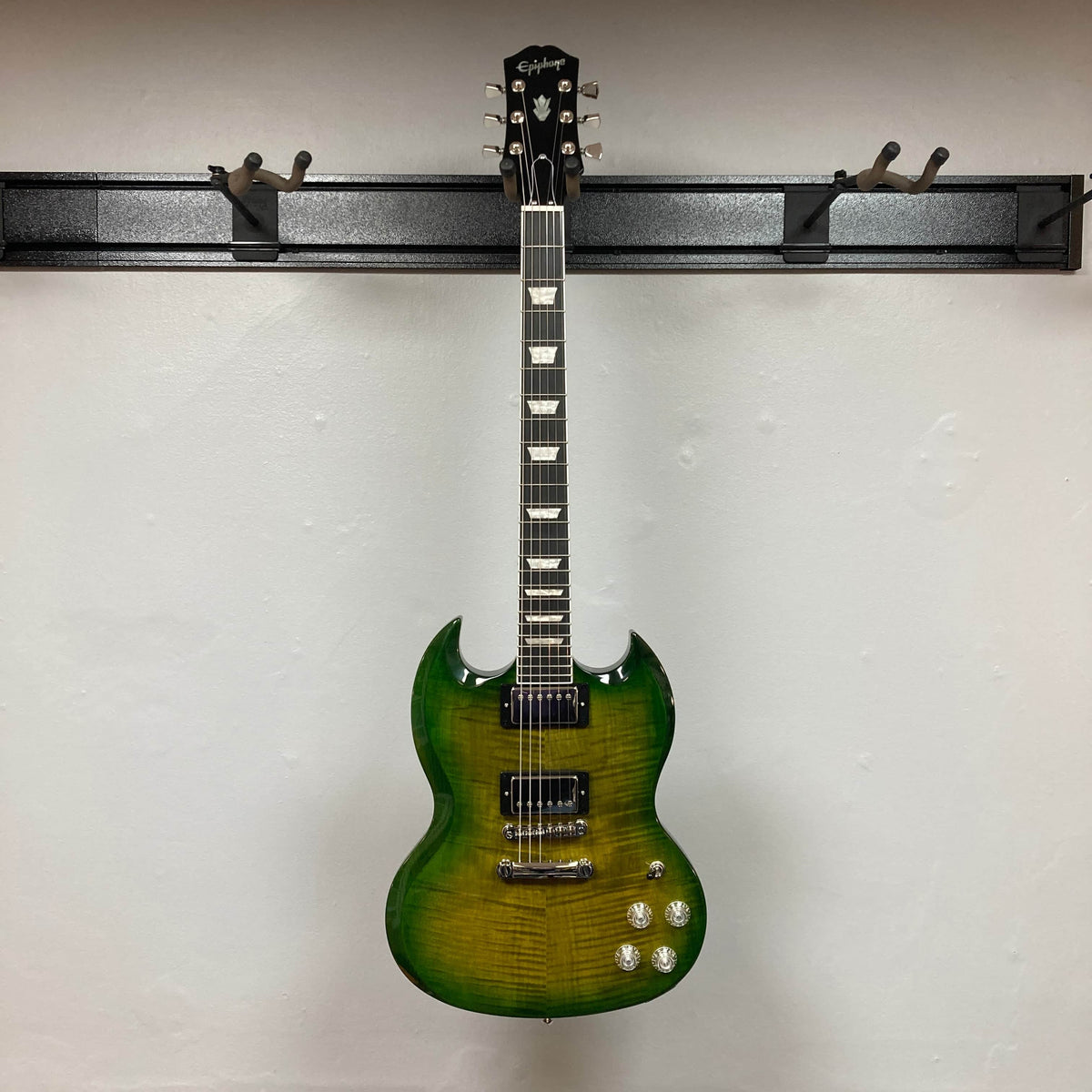 An Epiphone SG Modern Figured Iguana Burst electric guitar with a gig bag is hanging on a wall-mounted rack against a white background.
