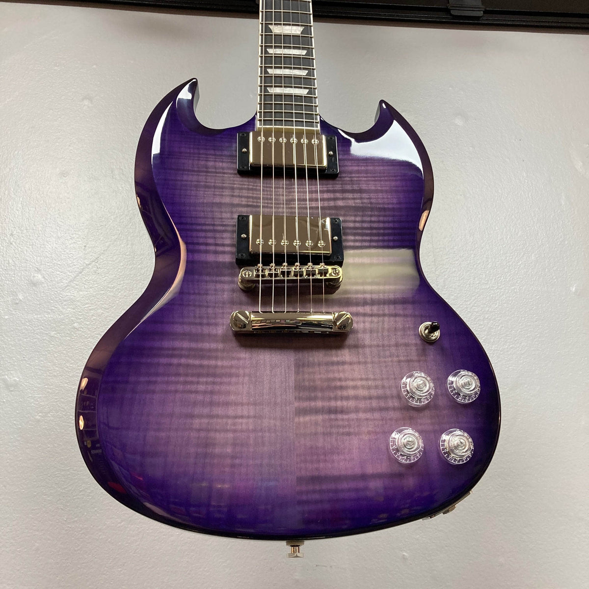 An Epiphone SG Modern Figured Purple Burst electric guitar with a flamed maple top, chrome hardware, ProBucker pickups, double cutaway body, four clear knobs, and selector switch is shown against a plain light-colored wall. Comes with GigBag.