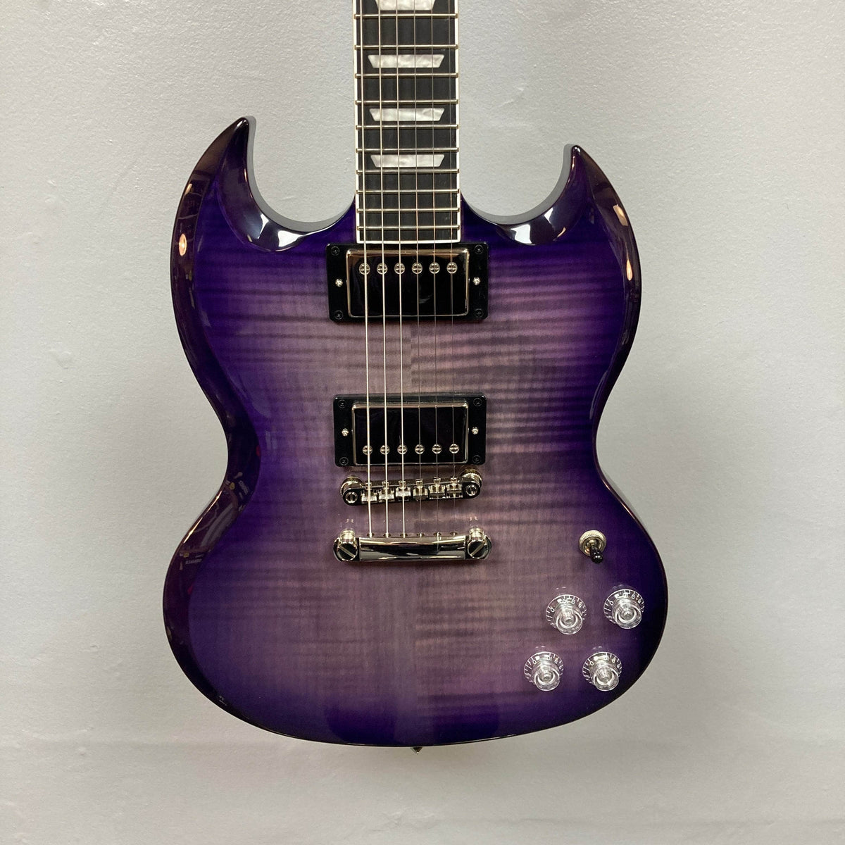 The Epiphone SG Modern Figured Purple Burst w/GigBag electric guitar, featuring a double-cutaway body, ProBucker humbucker pickups, four control knobs, and a three-way switch, is pictured against a plain light-colored wall.