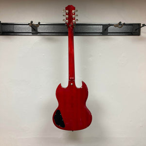 An Epiphone SG Standard Cherry w/Gigbag by Epiphone hangs on a black wall-mounted rack with its back facing outward, showcased against a white wall.