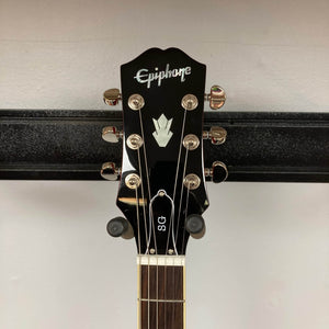 The Epiphone SG Standard Cherry w/Gigbag by Epiphone features a headstock with six tuning pegs, mounted on a black wall hanger. Inspired by the Gibson Collection, it has a mahogany body for classic rock style.