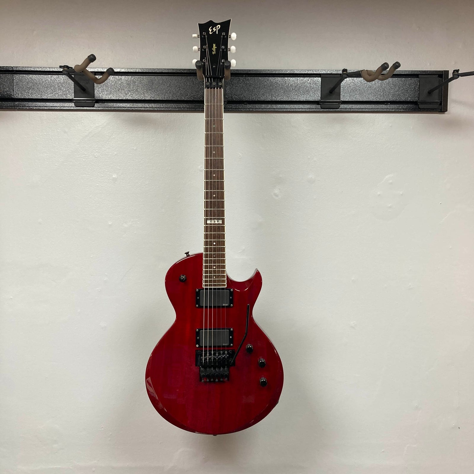 An ESP Standard Eclipse Transparent Cherry Red electric guitar with dual humbuckers, tremolo bridge, and four knobs is shown against a plain white wall. Includes case. Brand: Esp.