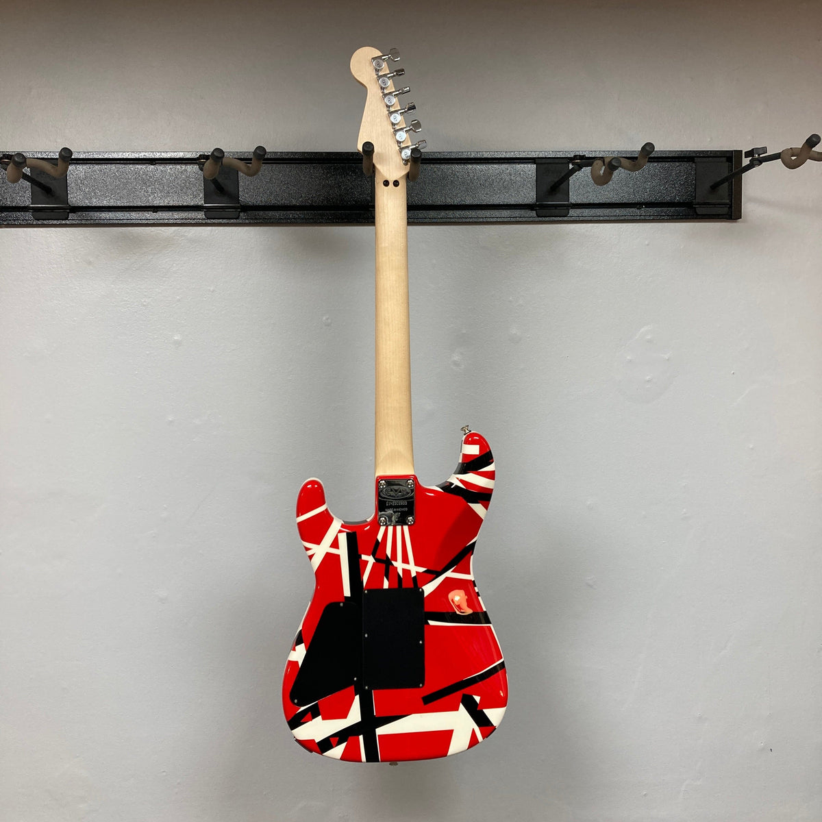 EVH Striped Series electric guitar with red, black, and white patterns hanging on a wall, perfect for enthusiasts at Guitars on Main.