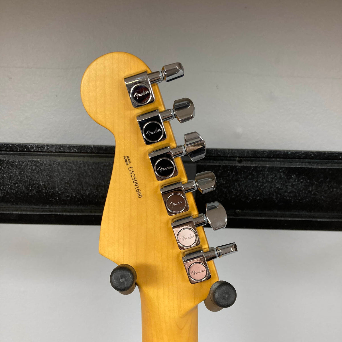 The back of a Fender American Professional II Stratocaster HSS in Dark Night headstock with six tuning pegs and "Fender" logos, displayed on a wall mount.