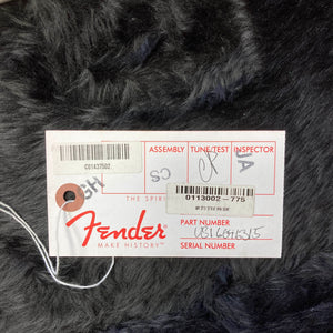 A white Fender inspection tag with handwritten signatures and numbers rests on a black fur-like surface, attached by a string—an authentic detail included with this Fender American Standard Strat upgraded Gilmour EMG DC-20 in the striking Bordeaux Metallic finish (w/Case, Used).
