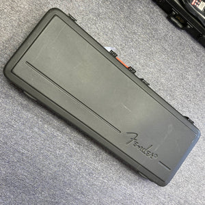 Black rectangular hard guitar case with "Fender" logo, lying closed on a gray carpeted floor—perfect for protecting your Fender American Standard Strat upgraded with Gilmour EMG DC-20 pickups in stunning Bordeaux Metallic.