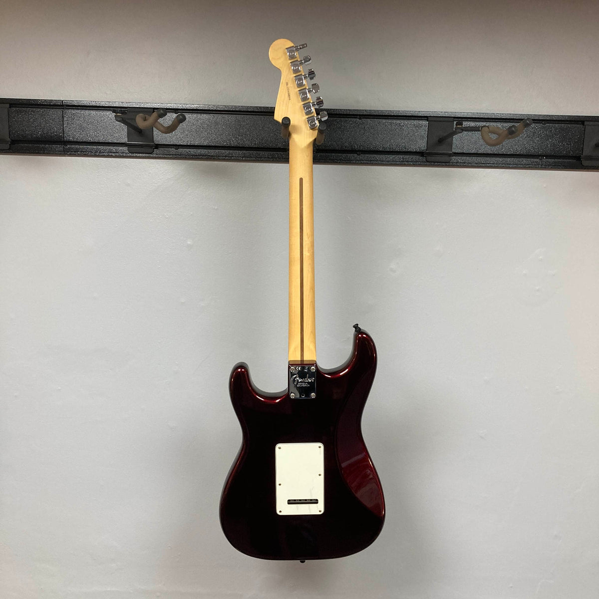 A striking Fender American Standard Strat upgraded Gilmour EMG DC-20 electric guitar in stunning Bordeaux Metallic is displayed on a wall-mounted rack, shown from the back with its neck pointing upward and the body downward. Outfitted with high-performance Gilmour EMG DC-20 pickups, this used Fender model comes complete with a case.