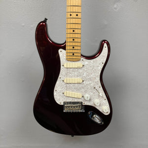 A Fender American Standard Strat in Bordeaux Metallic, upgraded with Gilmour EMG DC-20 pickups and featuring a maple neck and white pickguard, is mounted on a light gray wall.