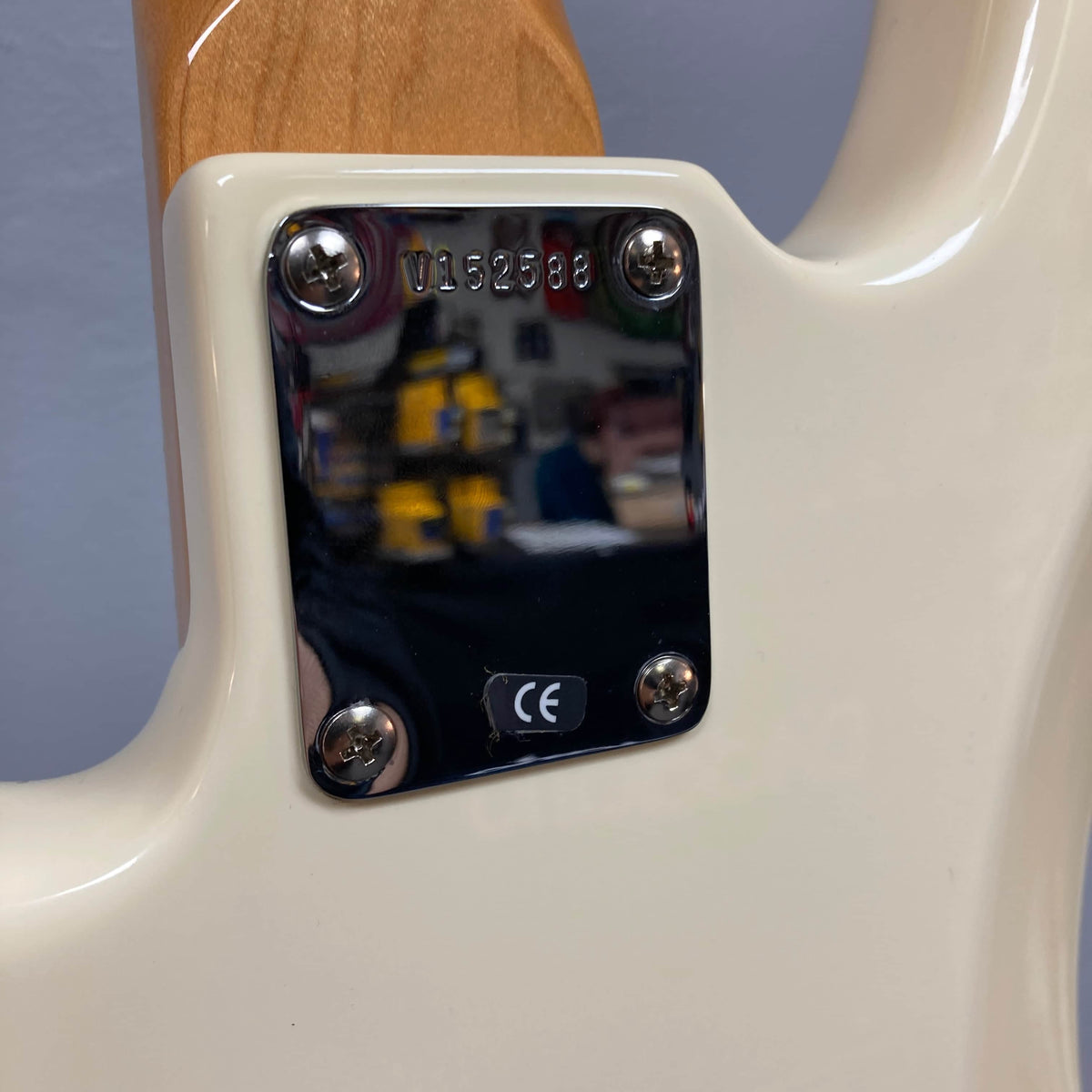 Close-up of the neck plate on a 2005 Fender American Vintage '62 Precision Bass in Olympic White, showing the serial number, four screws, and CE sticker. Includes case.