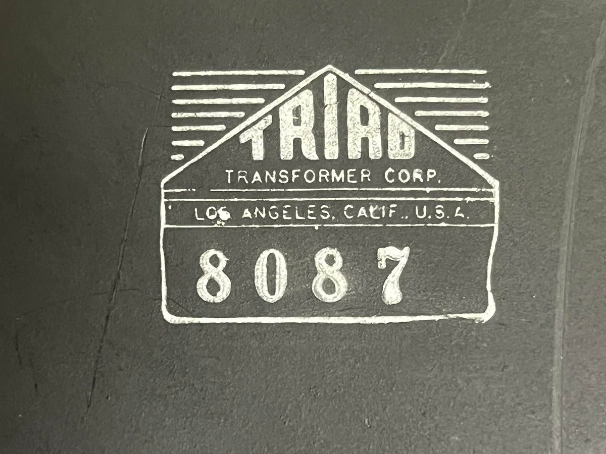 Logo for Triad Transformer Corp, address "Los Angeles, Calif., U.S.A." and number "8087" on a dark surface, as seen on vintage Fender 1957 Bassman 5F6 Narrow Panel 40-Watt 4x10" Guitar Combo w/Flight Case.