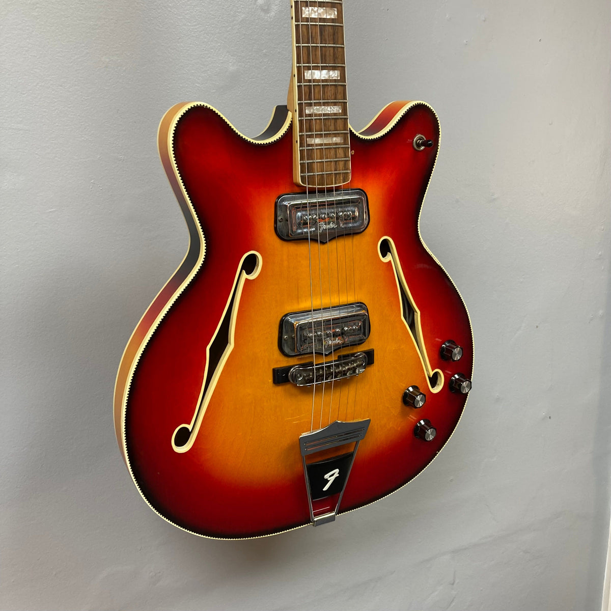 Fender Coronado II 1973 Sunburst guitar, semi-hollowbody design, dual Fideli&#39;Tron humbuckers, minor finish blemishes, displayed on a wall.