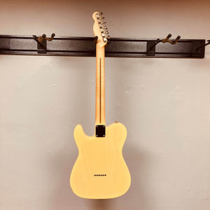 A Fender Custom Shop '51 Reissue Nocaster NOS 2006 electric guitar by Fender, in a light finish, hangs by its neck on a wall-mounted hook, displaying the back of the body and neck against a plain wall.