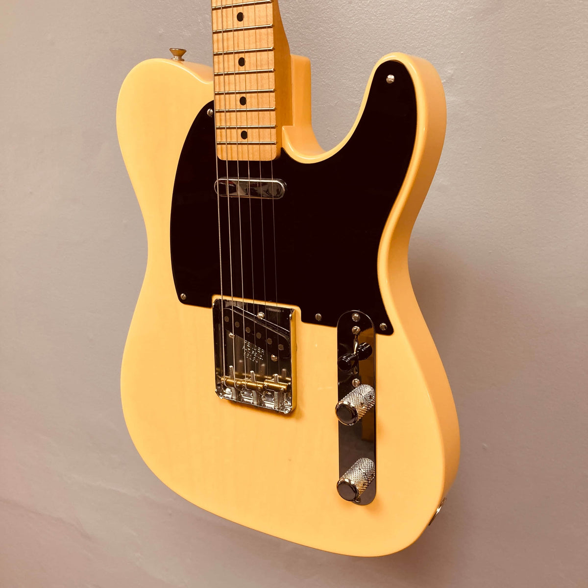 A Fender Custom Shop '51 Reissue Nocaster NOS 2006 electric guitar in yellow finish with a black pickguard, chrome hardware, and two control knobs is mounted on a plain light gray wall.