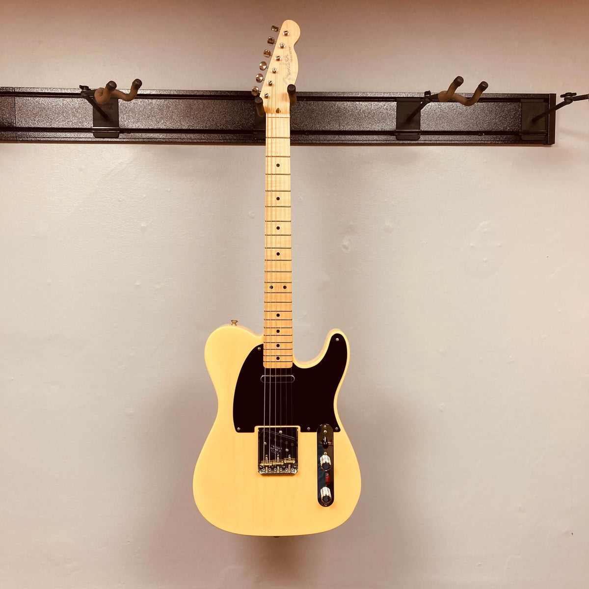 A cream Fender Custom Shop '51 Reissue Nocaster NOS 2006 electric guitar with a black pickguard hangs on a wall-mounted rack against a plain beige wall.
