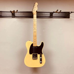 A cream Fender Custom Shop '51 Reissue Nocaster NOS 2006 electric guitar with a black pickguard hangs on a wall-mounted rack against a plain beige wall.