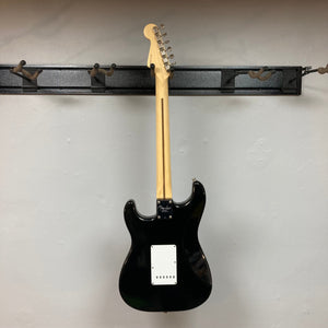 Fender Eric Clapton Artist Series Stratocaster USA 2001, black electric guitar, hanging on a wall hook, with included case and accessories.