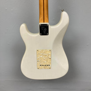 The back of a 2006 Fender Eric Johnson Stratocaster by Fender, featuring a light Maple Fingerboard neck, metal neck plate, and cream-colored back plate, set against a gray wall.