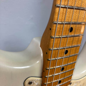 Close-up of a 2006 Fender Eric Johnson Stratocaster by Fender, showing the body, maple neck and fingerboard, and steel strings set against a light background.