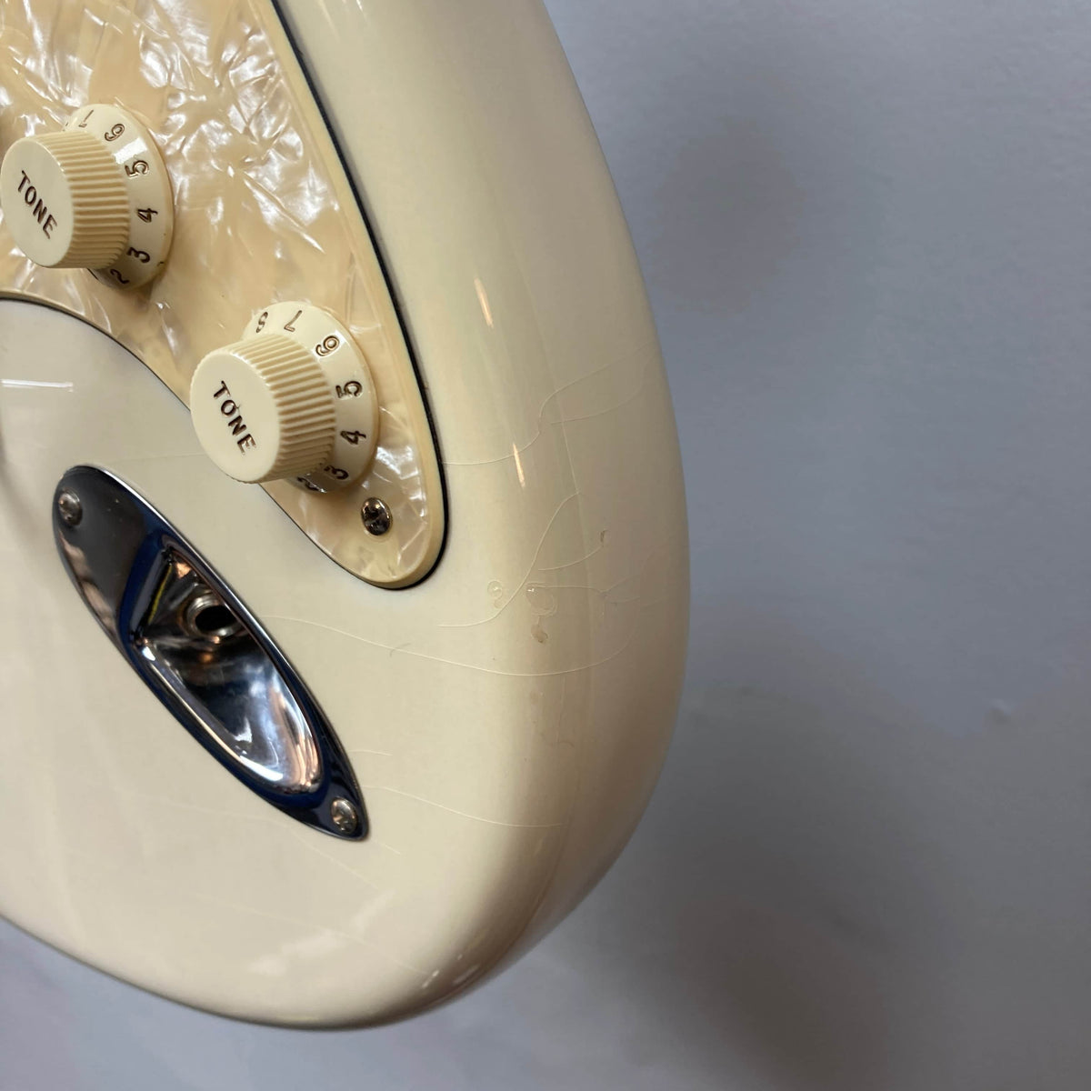 Close-up of a 2006 Fender Eric Johnson Stratocaster showing tone knobs, input jack, maple fingerboard, and visible surface cracks on the cream-colored body.