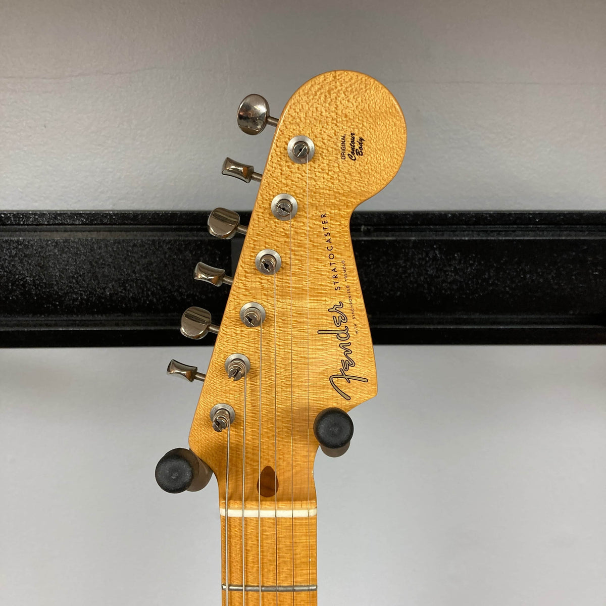 Close-up of the 2006 Fender Eric Johnson Stratocaster headstock by Fender, featuring tuning pegs, signature logo, and a section of the maple fingerboard against a plain wall.