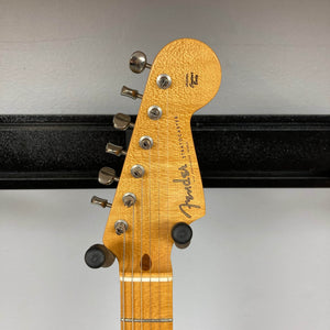 Close-up of the 2006 Fender Eric Johnson Stratocaster headstock by Fender, featuring tuning pegs, signature logo, and a section of the maple fingerboard against a plain wall.