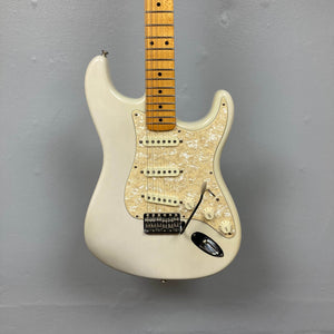 A 2006 Fender Eric Johnson Stratocaster in white with a maple fingerboard and pearl pickguard is displayed against a plain gray wall.